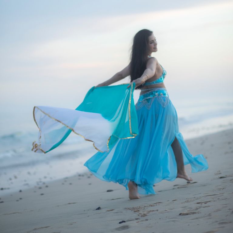 Frau im hellblauen orientalischen Kleid läuft fröhlich am Strand